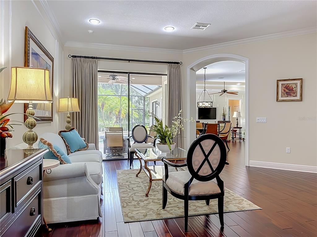 A living room features hardwood floors, a sofa, two accent chairs, and a sliding glass door — 7668 SILVERWOOD COURT, LAKEWOOD RANCH, FL