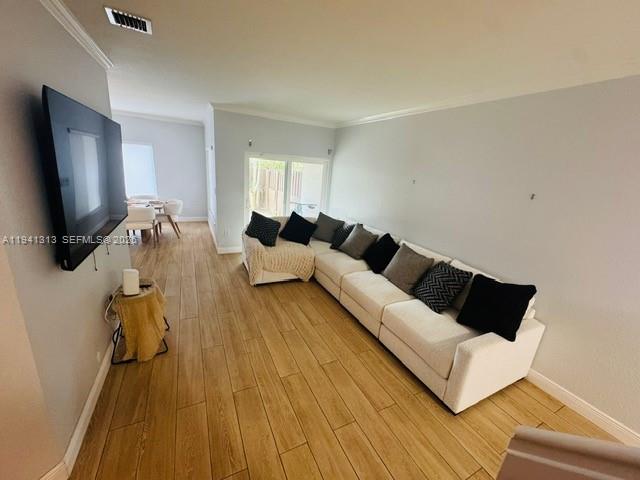 A living room features a large white sectional sofa, wood-look tile flooring, and a wall-mounted television — 10919 NW 67th Ter, Doral FL 33178, DORAL, FL