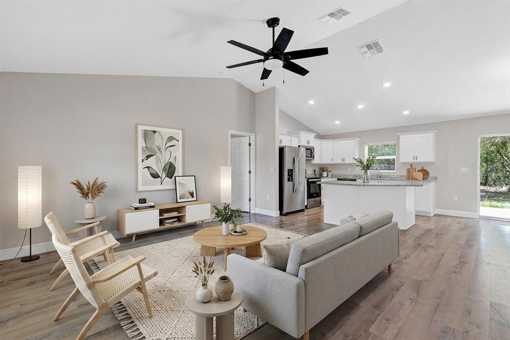 An open-concept living room and kitchen with vaulted ceilings, light wood flooring, and neutral decor — 5 LOCUST RADIAL CIRCLE, OCALA, FL