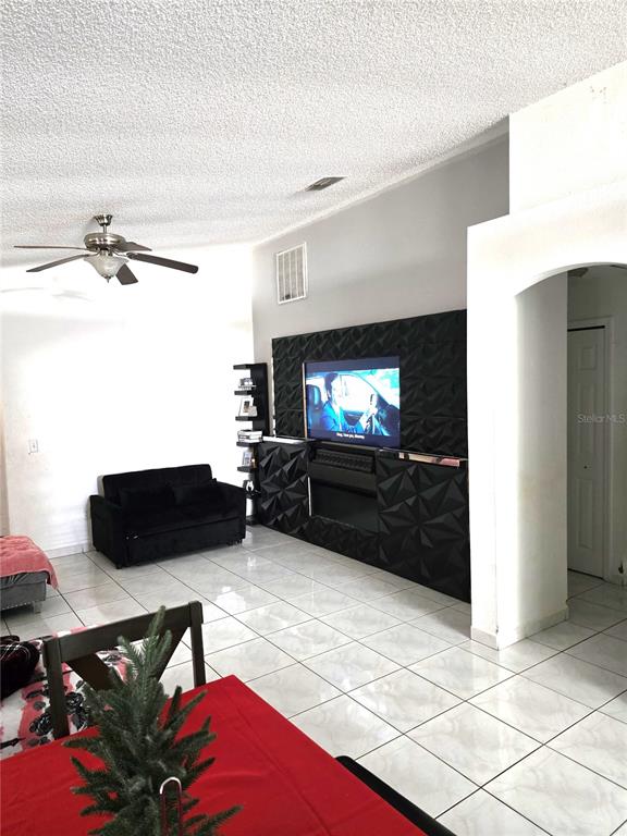 A living room features a black textured media wall, tiled floors, and gray tufted furniture — 2411 CONDADO COURT, KISSIMMEE, FL