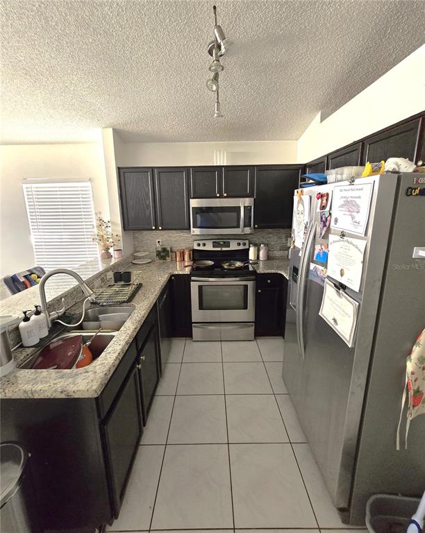 A kitchen features dark cabinets, granite countertops, stainless steel appliances, and two gray bar stools — 2411 CONDADO COURT, KISSIMMEE, FL