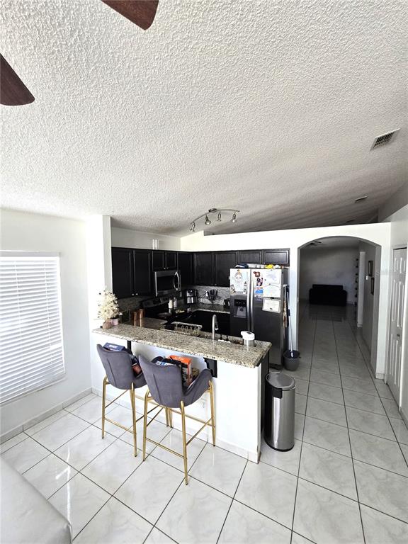 A living room with tile floors, a black sofa, a desk, and a sliding glass door — 2411 CONDADO COURT, KISSIMMEE, FL