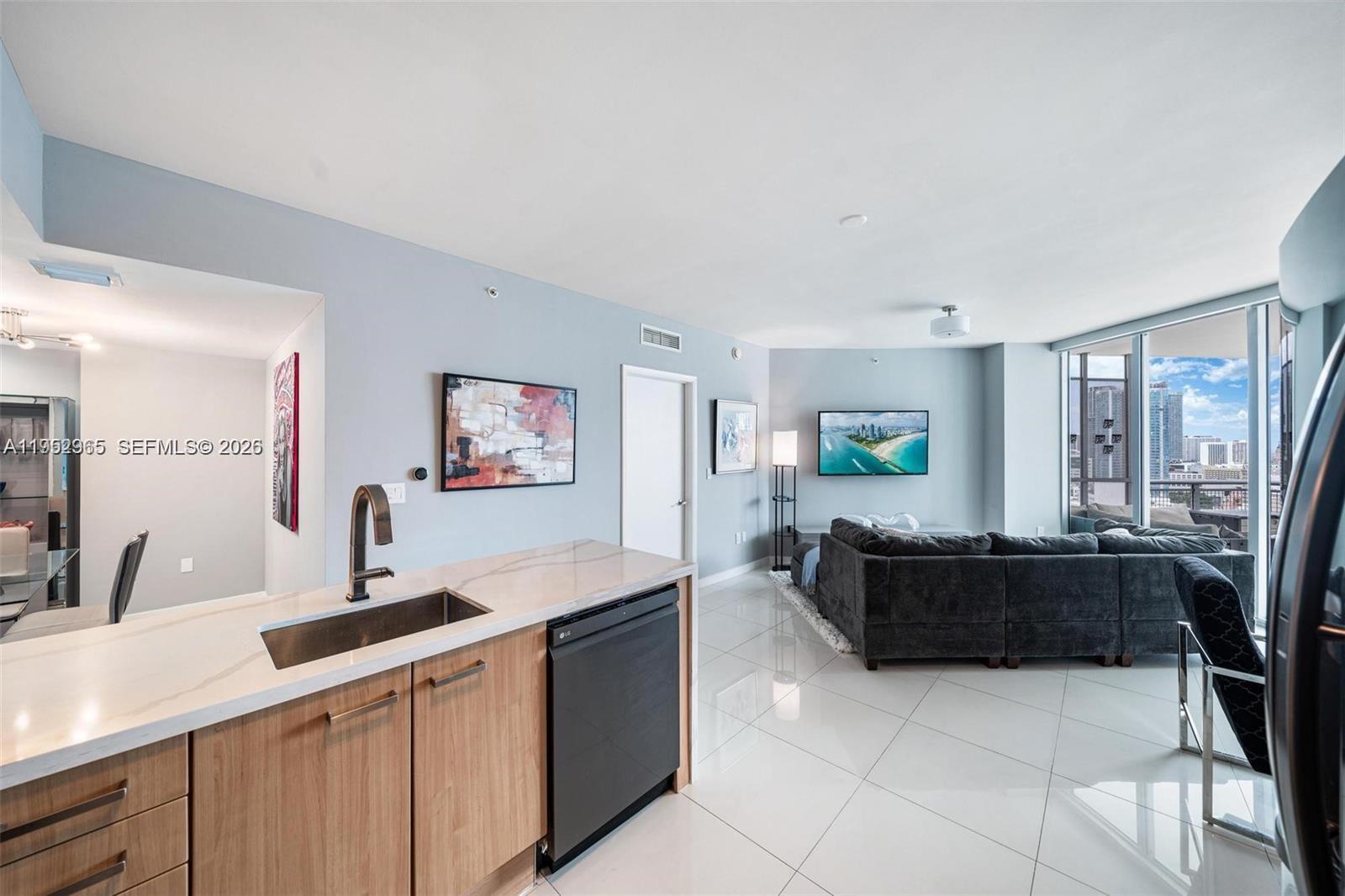 A modern kitchen with light wood cabinets and a white countertop overlooks a living area — 350 S Miami Ave # 2505, Miami FL 33130, MIAMI, FL