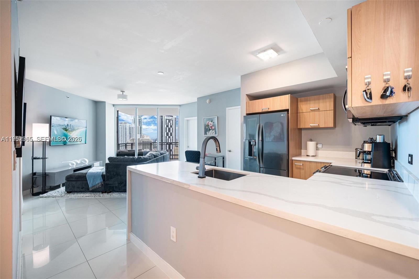 A modern kitchen with white countertops overlooks a living area with floor-to-ceiling windows — 350 S Miami Ave # 2505, Miami FL 33130, MIAMI, FL