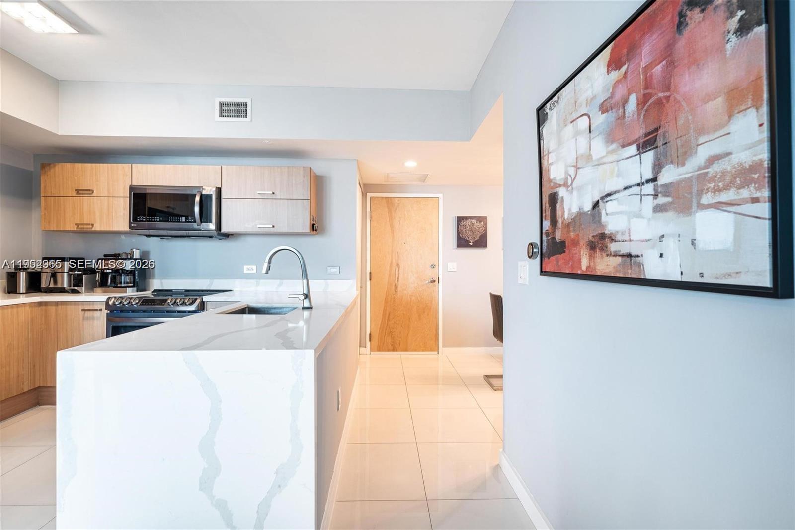 A modern kitchen features light wood cabinets, white quartz countertops, and a large island — 350 S Miami Ave # 2505, Miami FL 33130, MIAMI, FL