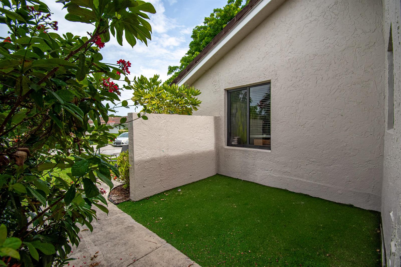 A small, private artificial turf courtyard sits beside a beige stucco house with a window — 22051 Montoya Drive, Boca Raton FL 33433, BOCA RATON, FL