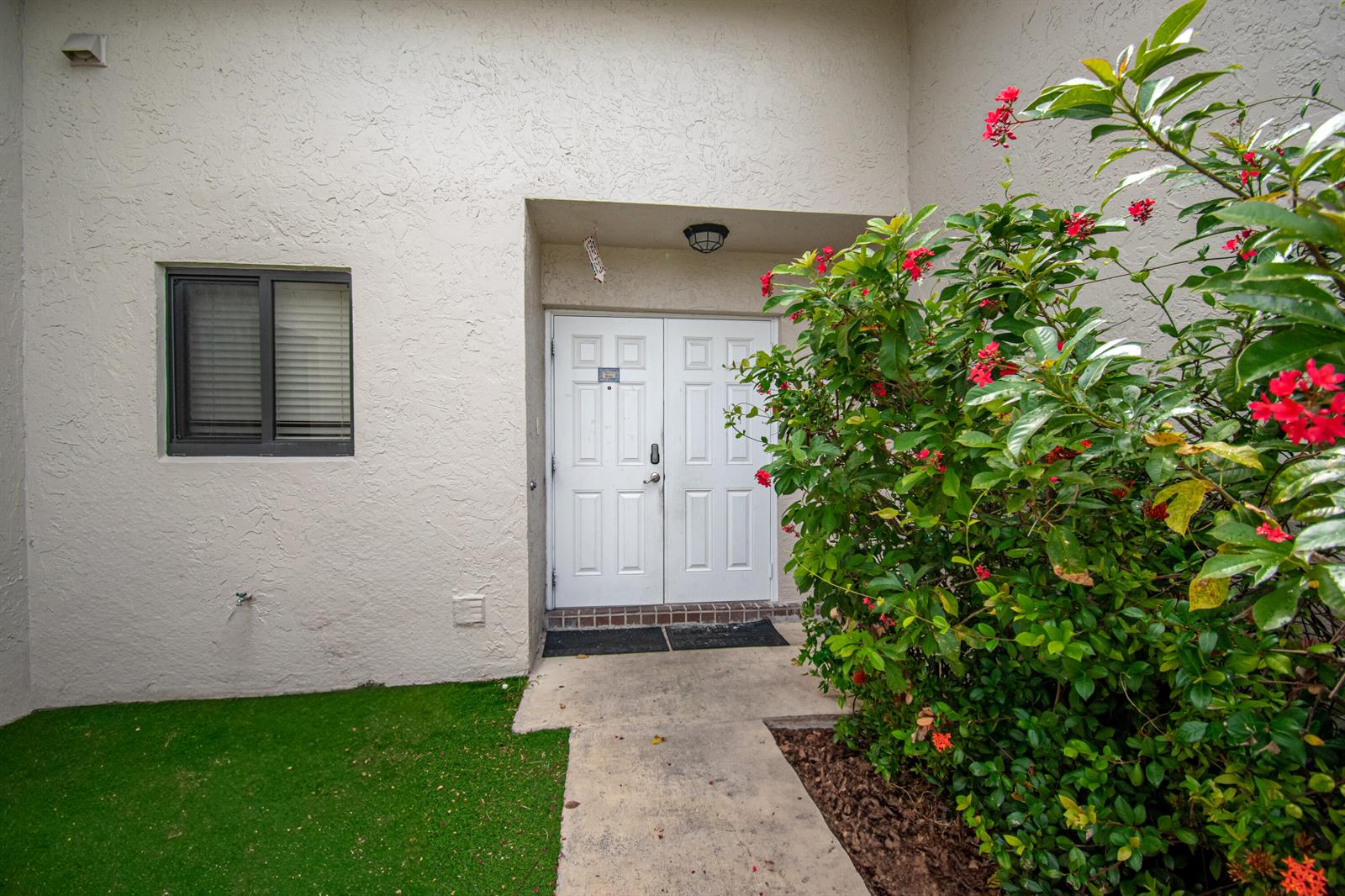 A white stucco exterior features a double front door, a window, and a flowering bush — 22051 Montoya Drive, Boca Raton FL 33433, BOCA RATON, FL