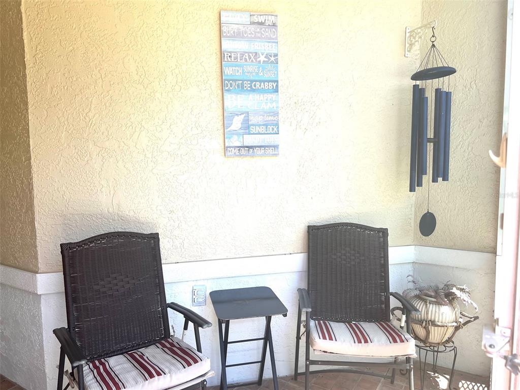 A covered porch features two wicker chairs, a small side table, and a decorative wall sign — 2602 EDGEWATER COURT, PALMETTO, FL