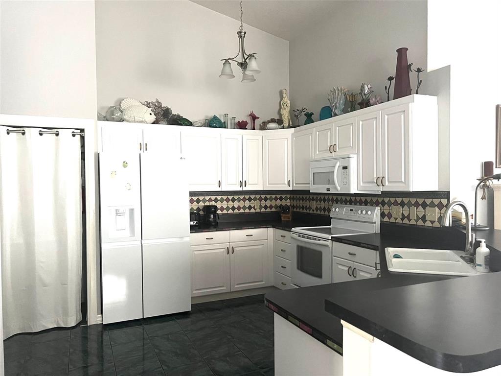 A kitchen with white cabinets, black countertops, a patterned backsplash, and dark tile flooring — 2602 EDGEWATER COURT, PALMETTO, FL