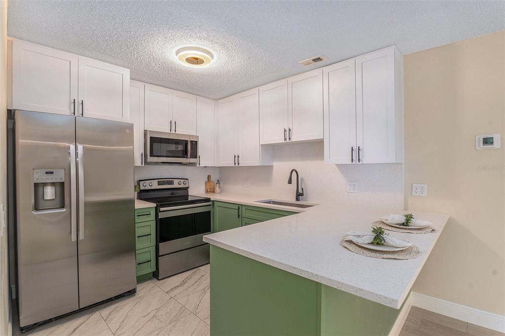 A kitchen features white upper cabinets, green lower cabinets, stainless steel appliances, and quartz countertops — 3822 CORTEZ DRIVE UNIT D, TAMPA, FL
