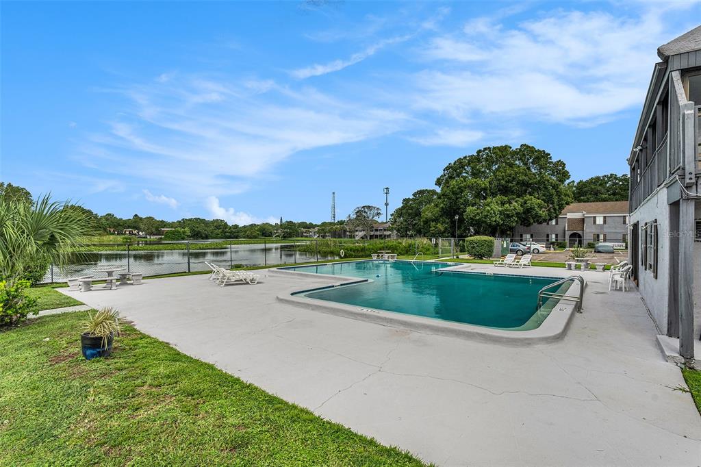 An outdoor swimming pool sits on a concrete deck next to a lake and apartments — 3822 CORTEZ DRIVE UNIT D, TAMPA, FL