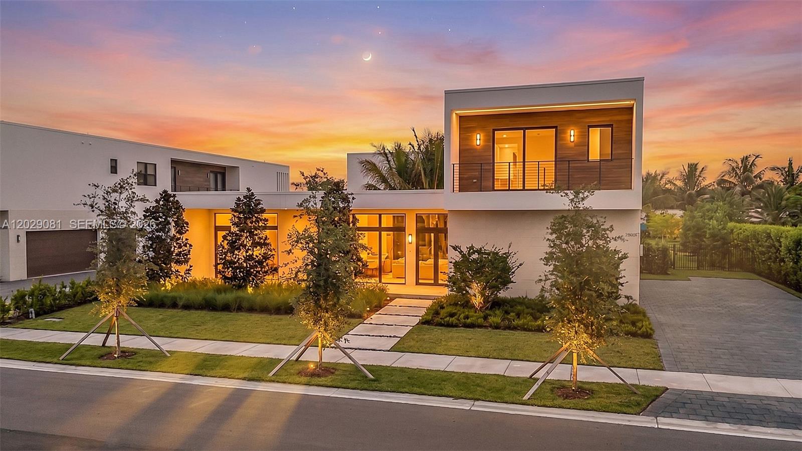 A modern two-story house with a flat roof, wood accents, and a paved driveway at dusk — 16689 N Botaniko Dr N, Weston FL 33326, WESTON, FL