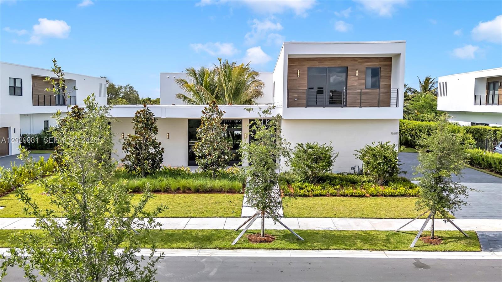 A modern two-story house features white exterior walls, wood-paneled accents, and a landscaped front yard — 16689 N Botaniko Dr N, Weston FL 33326, WESTON, FL