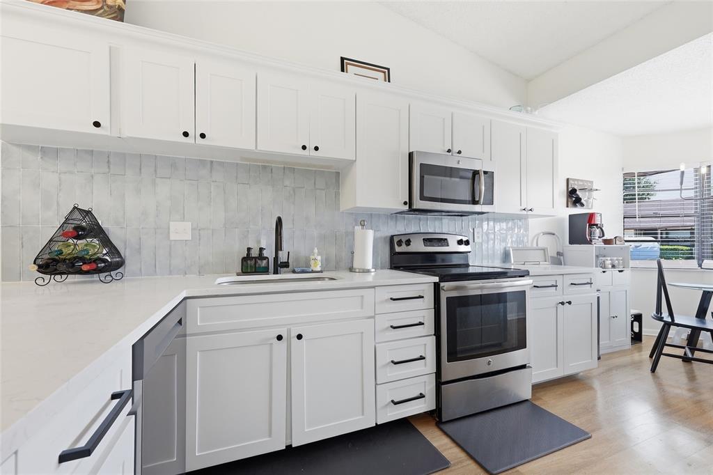 A kitchen features white cabinets, stainless steel appliances, a light-colored backsplash, and quartz countertops — 250 HOMEWOOD AVENUE UNIT 11A, DEBARY, FL
