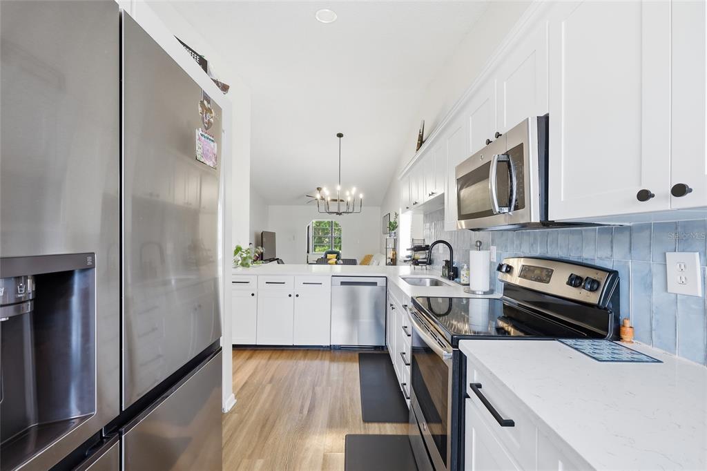 A kitchen with white cabinets, stainless steel appliances, and a view into the living area — 250 HOMEWOOD AVENUE UNIT 11A, DEBARY, FL