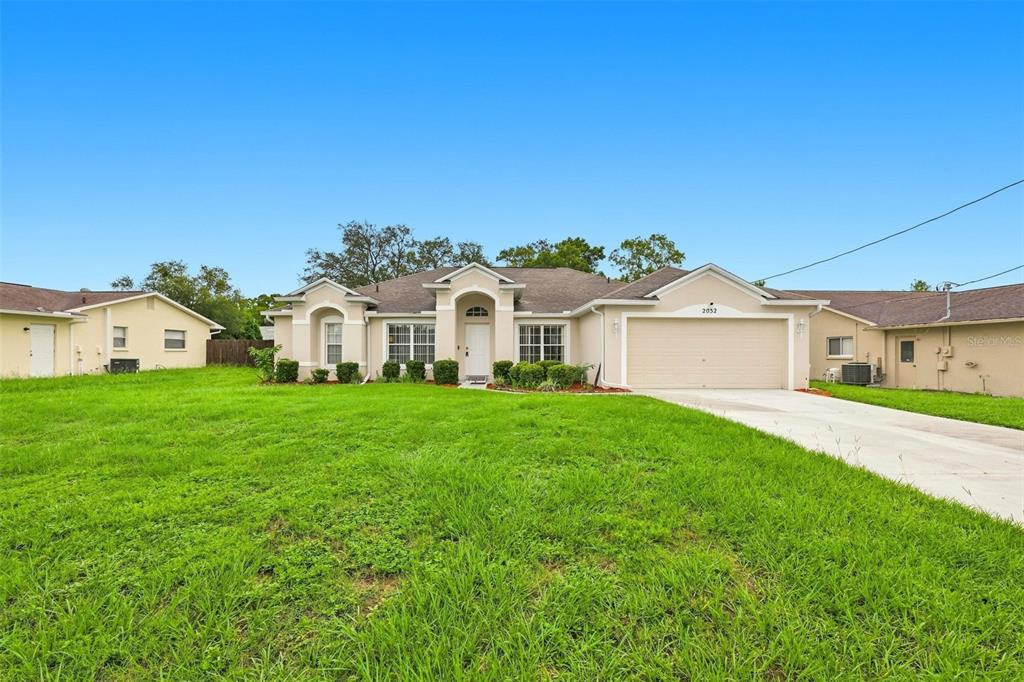 A single-story suburban house with a beige stucco exterior and a two-car garage — 2032 DE CARLO AVENUE, SPRING HILL, FL