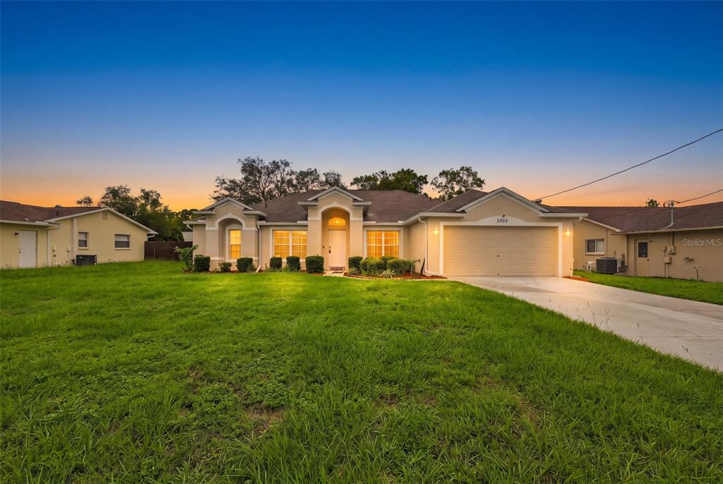 A single-story suburban house with a beige stucco exterior, a two-car garage, and a lawn — 2032 DE CARLO AVENUE, SPRING HILL, FL