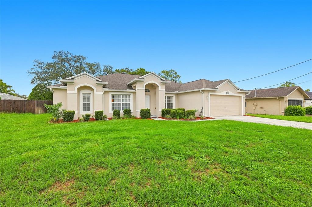 A single-story house with a beige exterior, a two-car garage, and a large front lawn — 2032 DE CARLO AVENUE, SPRING HILL, FL