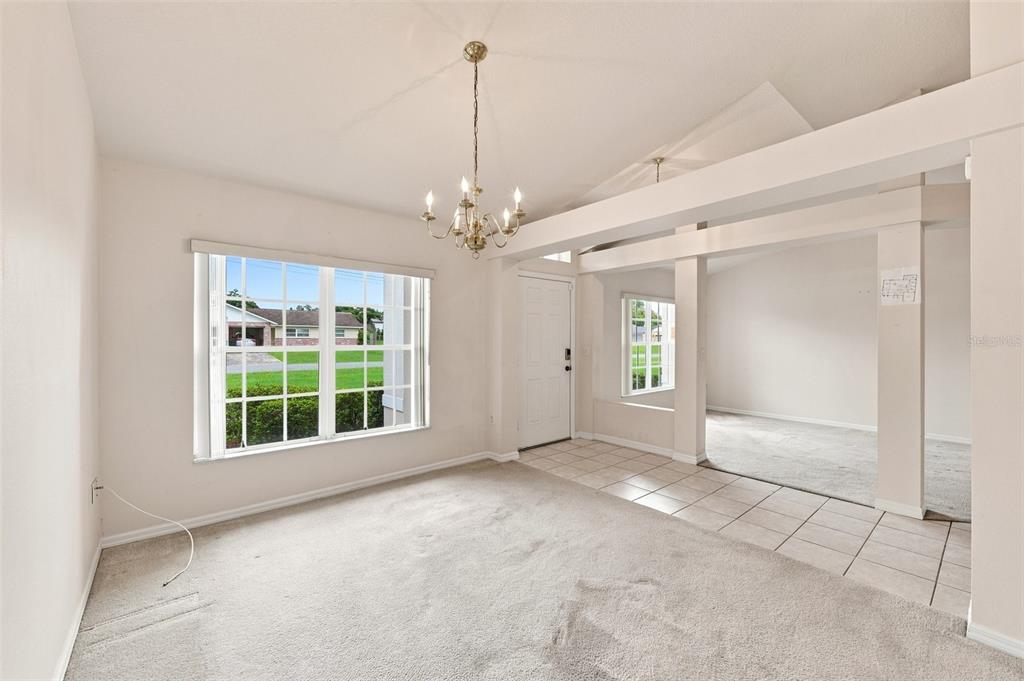 A carpeted dining area with a chandelier and a tiled entryway leading to another room — 2032 DE CARLO AVENUE, SPRING HILL, FL