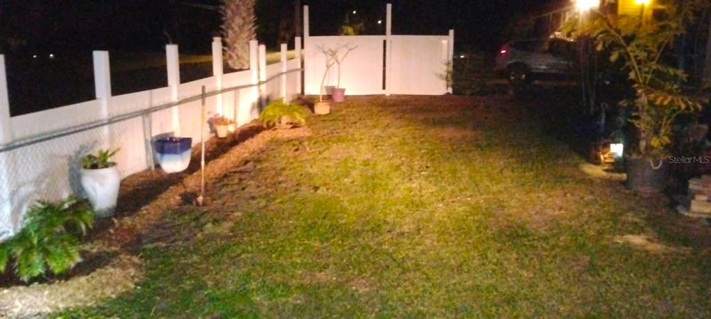 A backyard at night features a white vinyl fence, potted plants, and a grassy lawn — 15373 ORCHID DRIVE, PUNTA GORDA, FL