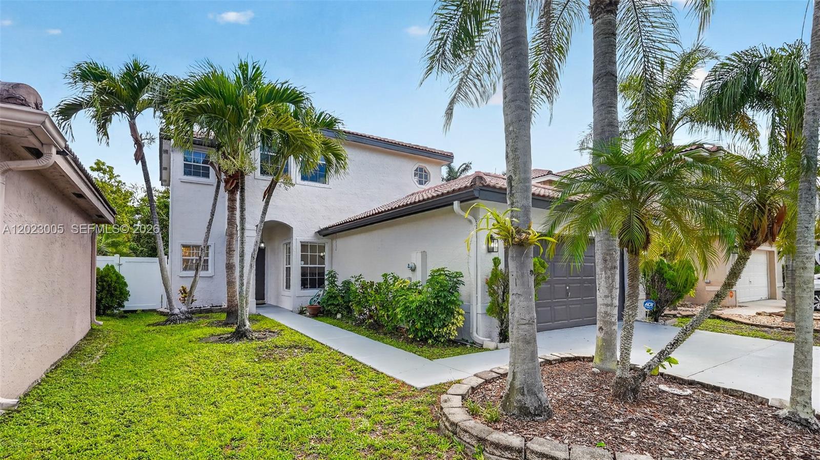 A two-story white stucco house features a gray garage door and palm trees — 17731 SW 23rd St, Miramar FL 33029, MIRAMAR, FL