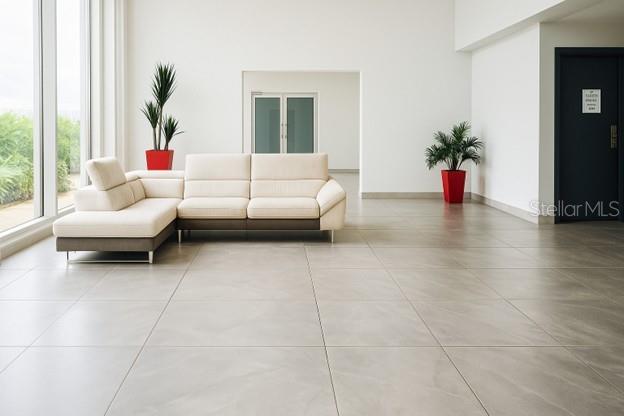 A modern, minimalist lobby features a beige sectional sofa, large floor tiles, and two potted plants — 3103 AVE. ISLA VERDE COND. CONDESA DEL MAR UNIT 1402, ISLA VERDE, PR