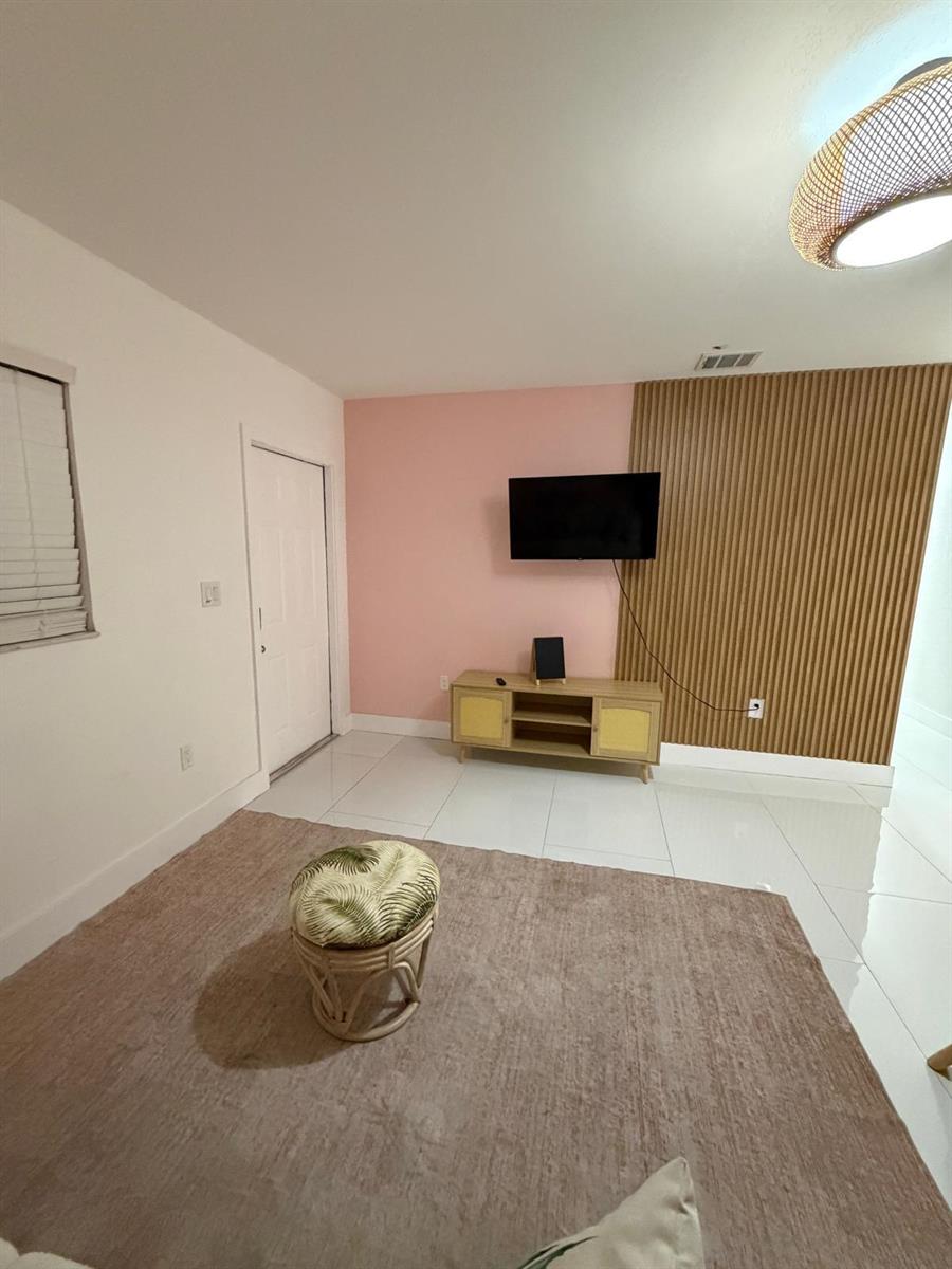 A living room features a pink accent wall, wood slat paneling, and a television console — 1700 NE 146th Street, Miami FL 33181, MIAMI, FL