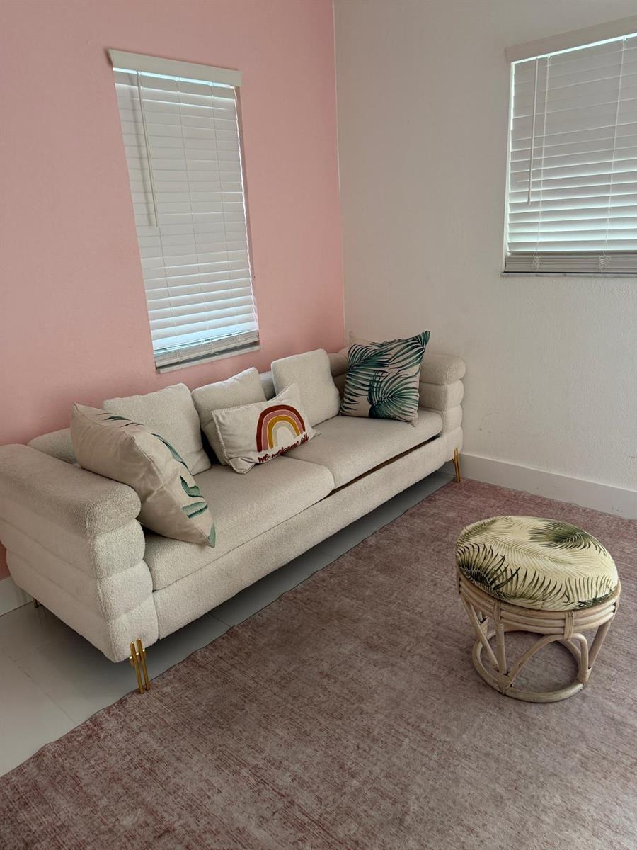 A living room features a cream-colored sofa, a round rattan stool, and a pink accent wall — 1700 NE 146th Street, Miami FL 33181, MIAMI, FL