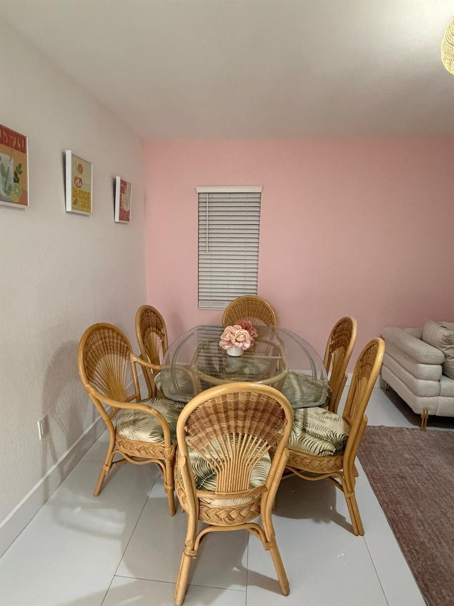 A dining room features a glass-topped rattan table with six chairs against a pink wall — 1700 NE 146th Street, Miami FL 33181, MIAMI, FL