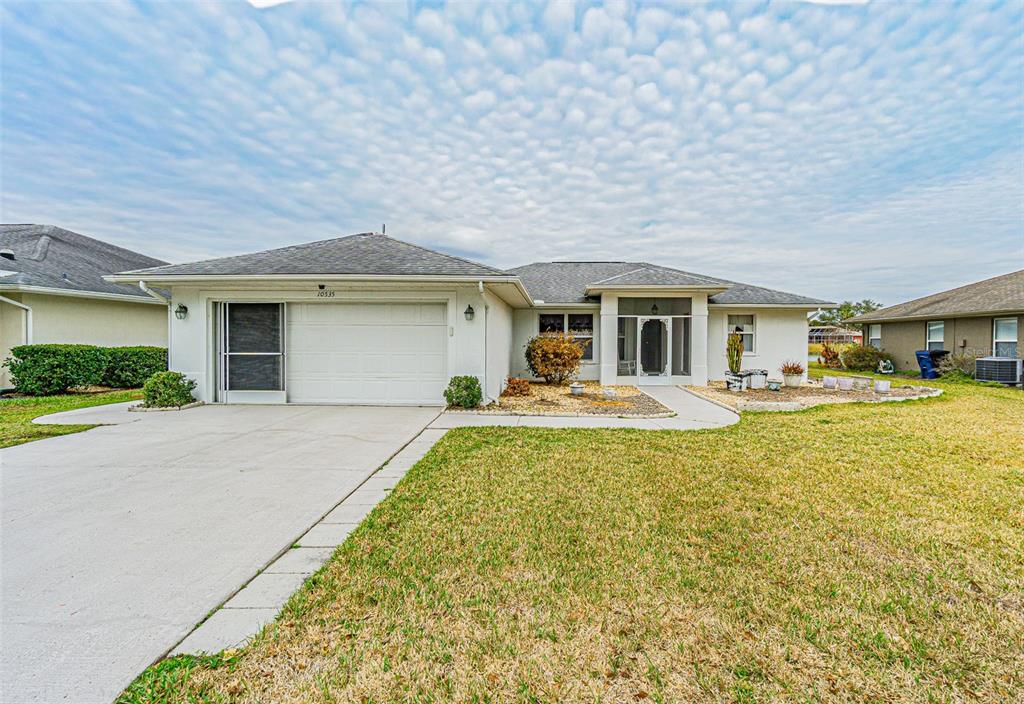 A single-story suburban house with a two-car garage, light-colored stucco exterior, and a screened entryway — 10535 MOSHIE LANE, SAN ANTONIO, FL