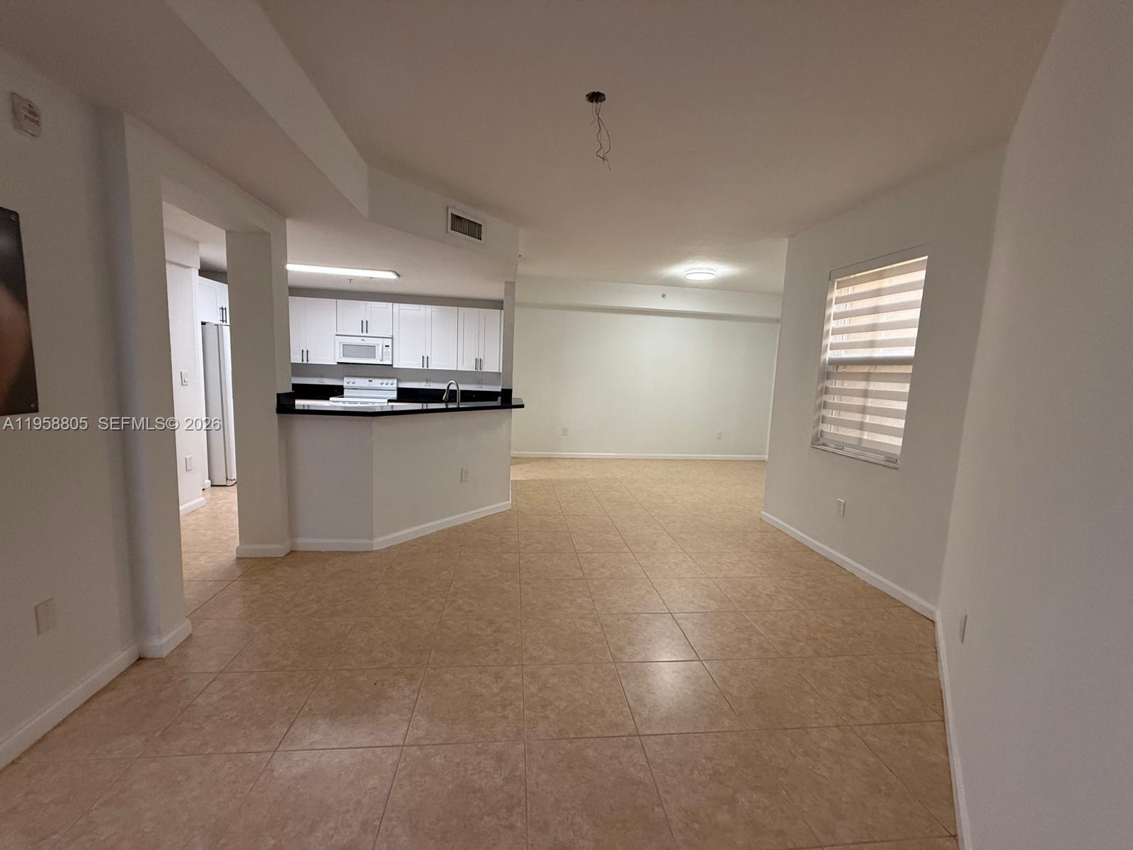 An open-concept living area features beige tile flooring, white walls, and a kitchen with white cabinets — 11603 NW 89th St # 215, Doral FL 33178, DORAL, FL