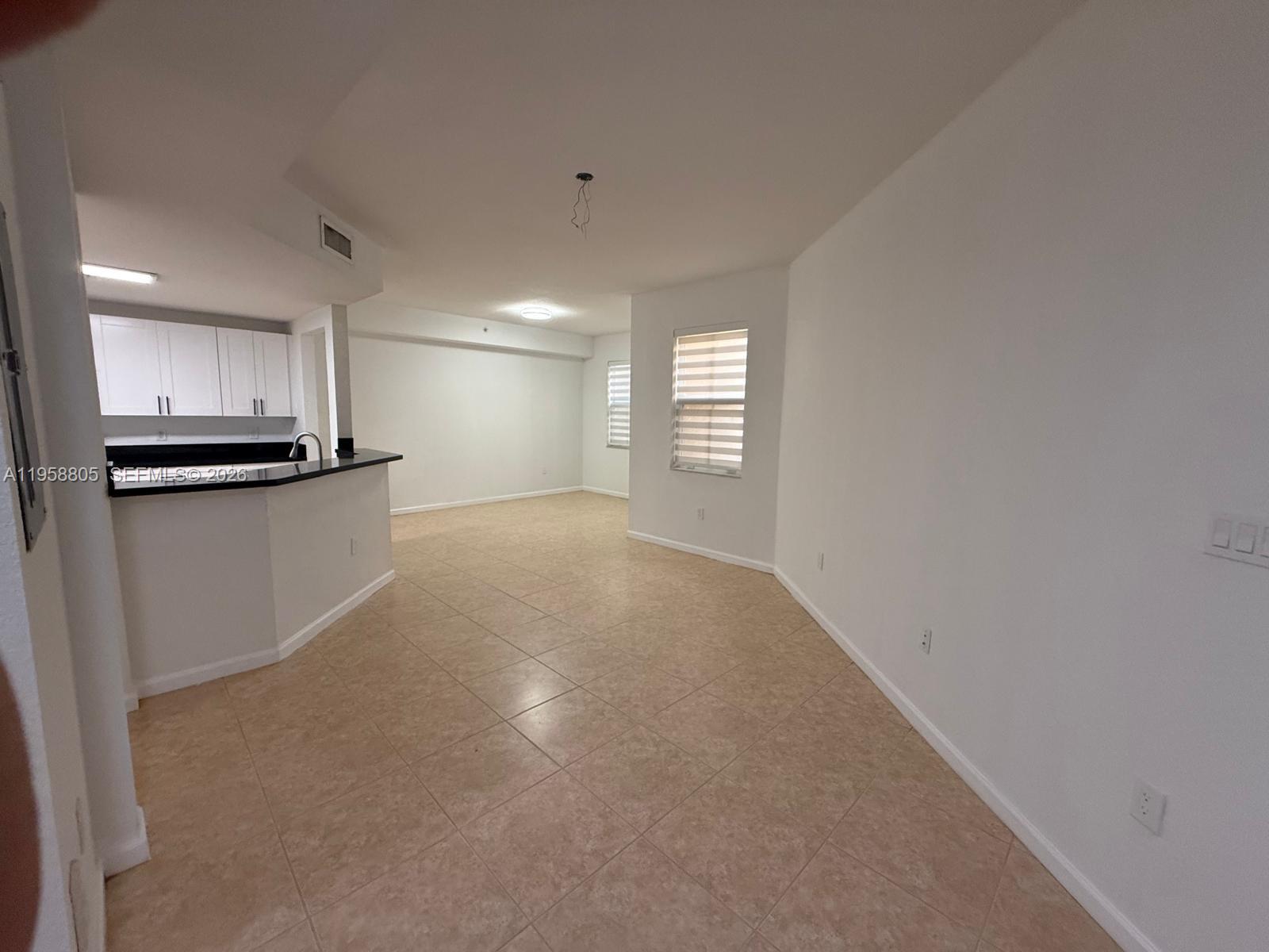 An open-concept living area features light-colored tile floors, white walls, and a kitchen peninsula — 11603 NW 89th St # 215, Doral FL 33178, DORAL, FL