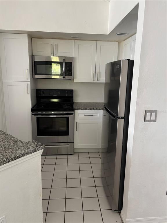 A kitchen features white cabinets, stainless steel appliances, granite countertops, and white floor tiles — 4642 COMMANDER DRIVE UNIT 938, ORLANDO, FL