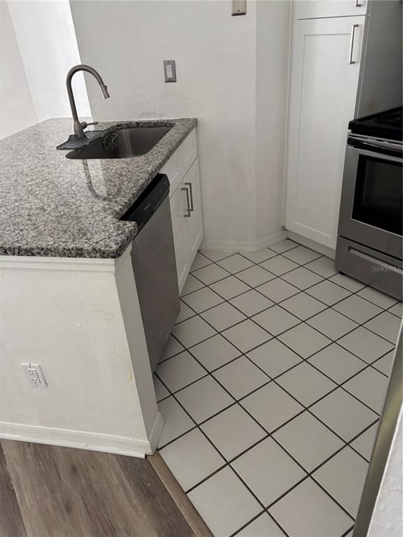 A kitchen features granite countertops, a stainless steel sink, a dishwasher, and white tile flooring — 4642 COMMANDER DRIVE UNIT 938, ORLANDO, FL