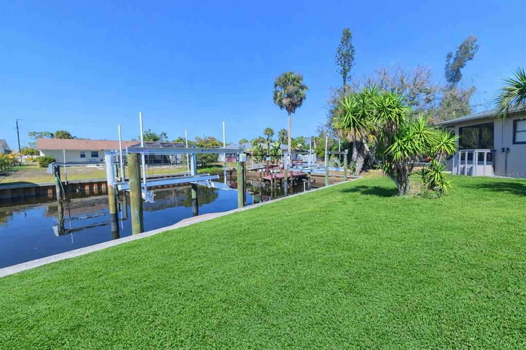 A grassy backyard features a boat lift over a canal with houses in the background — 3211 RIVERSIDE DRIVE, PUNTA GORDA, FL