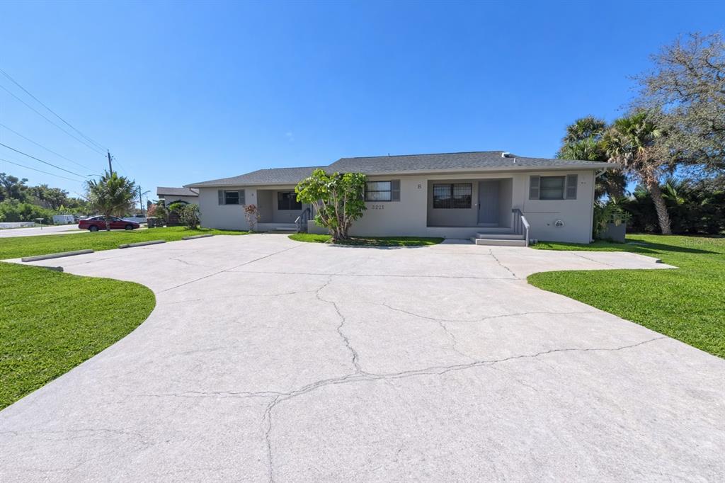 A single-story duplex building features a large concrete parking area and a grassy lawn — 3211 RIVERSIDE DRIVE, PUNTA GORDA, FL