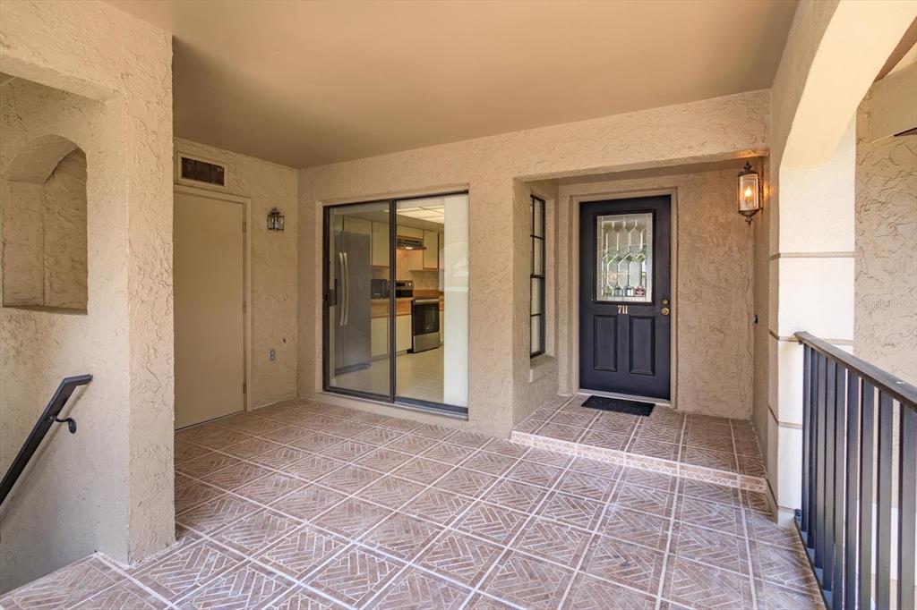 A tiled patio features a dark front door, a sliding glass door, and a metal railing — 1055 KENSINGTON PARK DRIVE UNIT 711, ALTAMONTE SPRINGS, FL