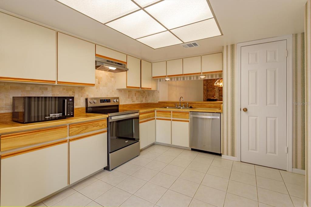 A kitchen features white cabinets with wood trim, stainless steel appliances, and light-colored tile flooring — 1055 KENSINGTON PARK DRIVE UNIT 711, ALTAMONTE SPRINGS, FL