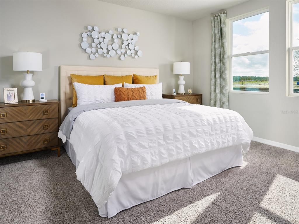 A bedroom features a bed with white bedding, yellow pillows, and two wooden nightstands — 895 SUNSHOWER DRIVE, LADY LAKE, FL