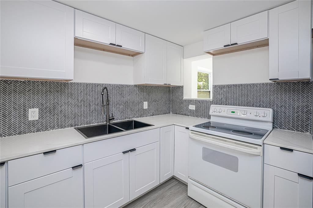 A kitchen features white cabinets, a dark herringbone backsplash, a black sink, and white appliances — 203 WATERWAY CIRCLE NE, PORT CHARLOTTE, FL