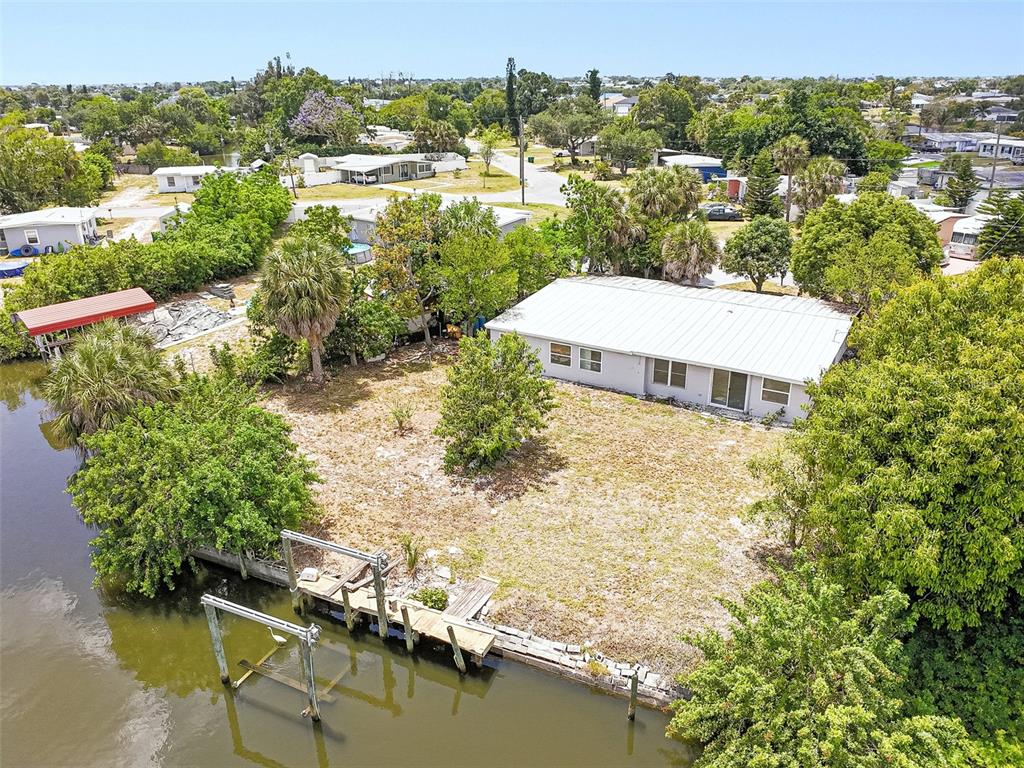 An aerial view shows a house with a metal roof, a yard, and a boat dock — 203 WATERWAY CIRCLE NE, PORT CHARLOTTE, FL