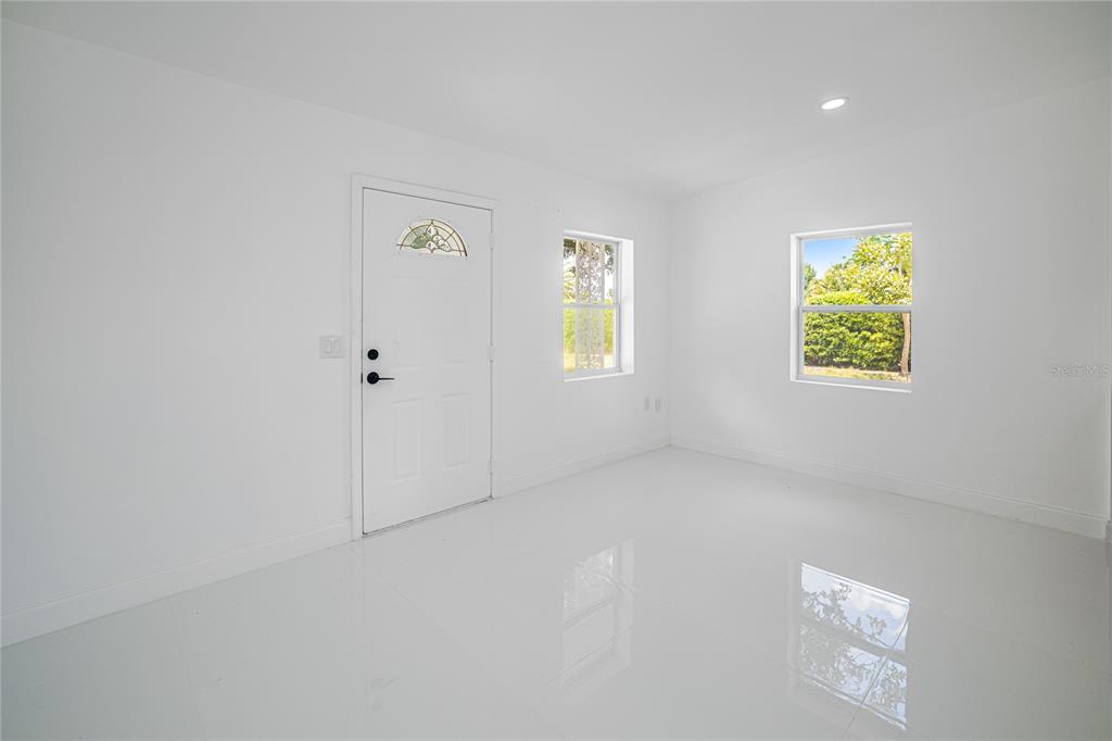 A bright, empty room features white walls, glossy tile flooring, a front door, and two windows — 203 WATERWAY CIRCLE NE, PORT CHARLOTTE, FL
