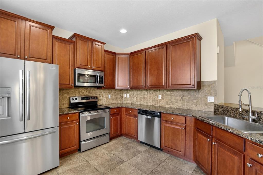 A kitchen with wood cabinets, stainless steel appliances, granite countertops, and a tiled backsplash — 714 ASHENTREE DRIVE, PLANT CITY, FL