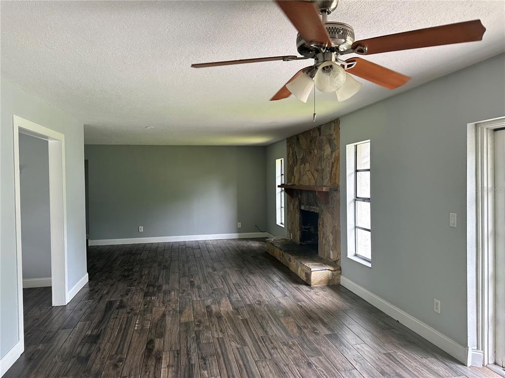 A living room with wood-look tile flooring, a stone fireplace, and a ceiling fan — 5020 NE 7TH STREET, OCALA, FL