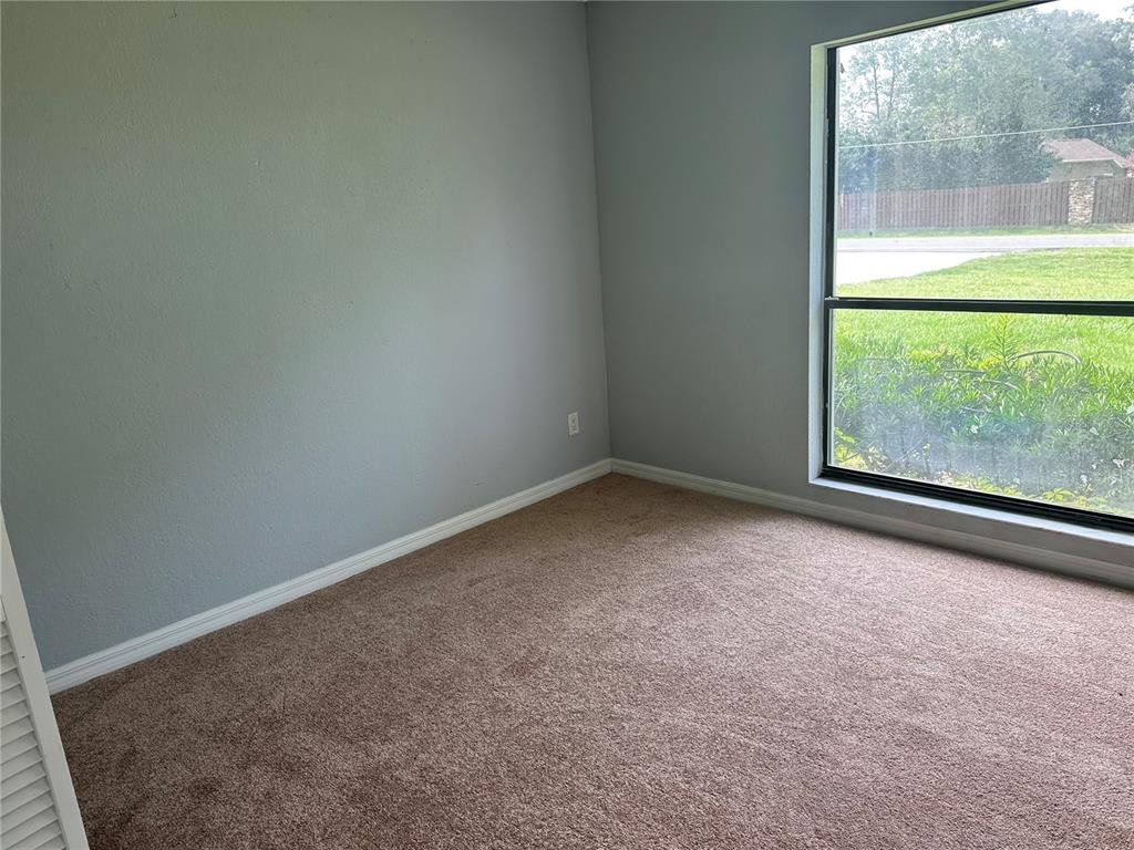 An empty bedroom with gray walls, brown carpet, and a large window overlooking a yard — 5020 NE 7TH STREET, OCALA, FL