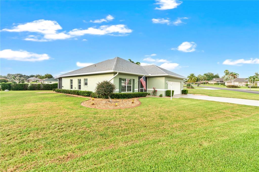 A light green single-story house with a gray roof and an American flag — 117 ROSEWOOD DRIVE N, LAKE PLACID, FL