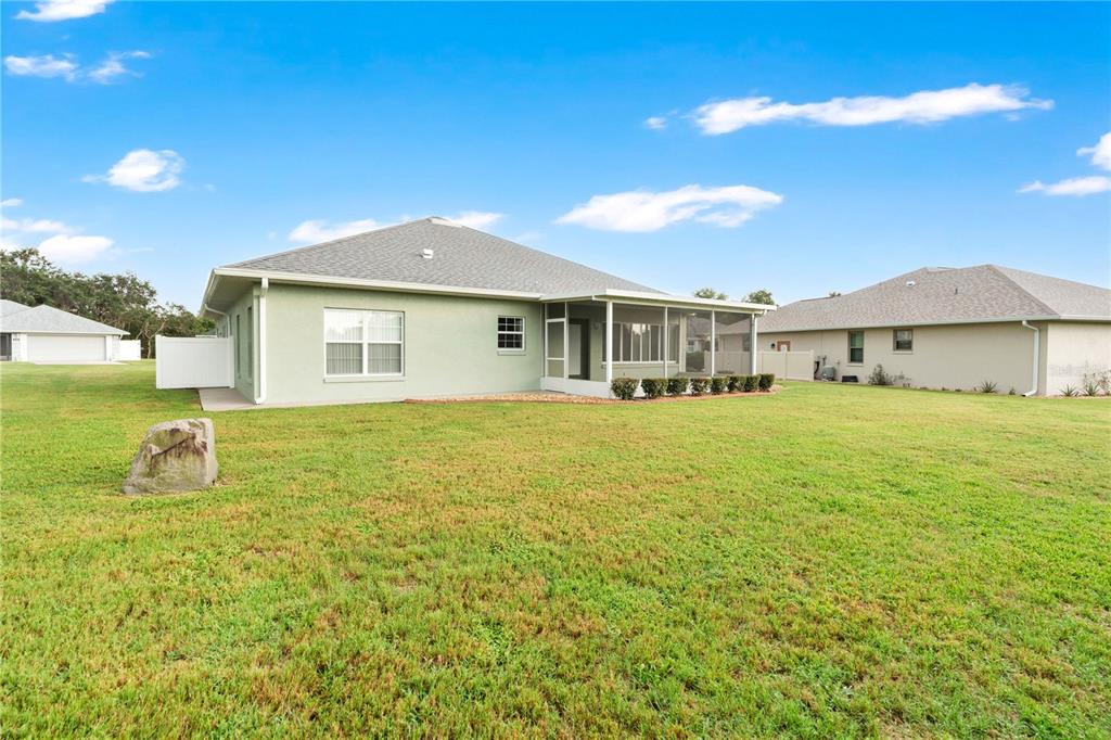 The rear exterior of a light green house features a screened-in porch and large lawn — 117 ROSEWOOD DRIVE N, LAKE PLACID, FL