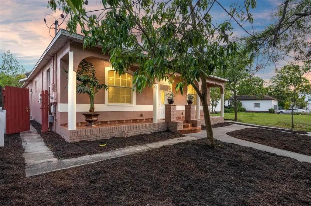 A single-story house with a covered front porch, tan stucco walls, and a red fence — 2324 W PALMETTO STREET, TAMPA, FL