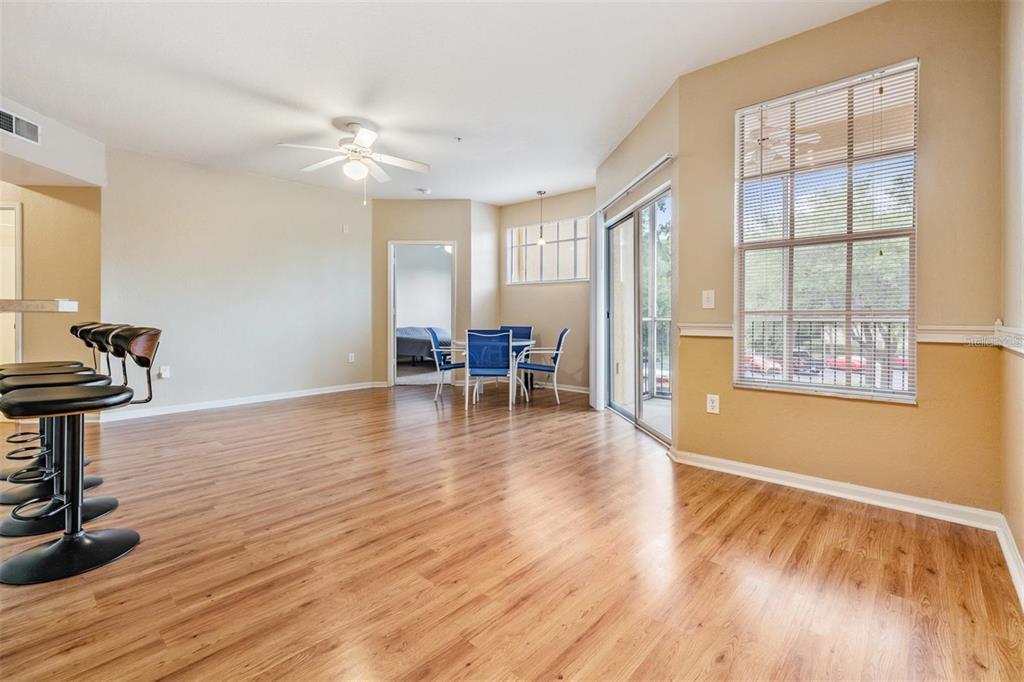 An open-concept dining and living area features wood-look flooring, a ceiling fan, and sliding doors — 5125 PALM SPRINGS BOULEVARD UNIT 8203, TAMPA, FL