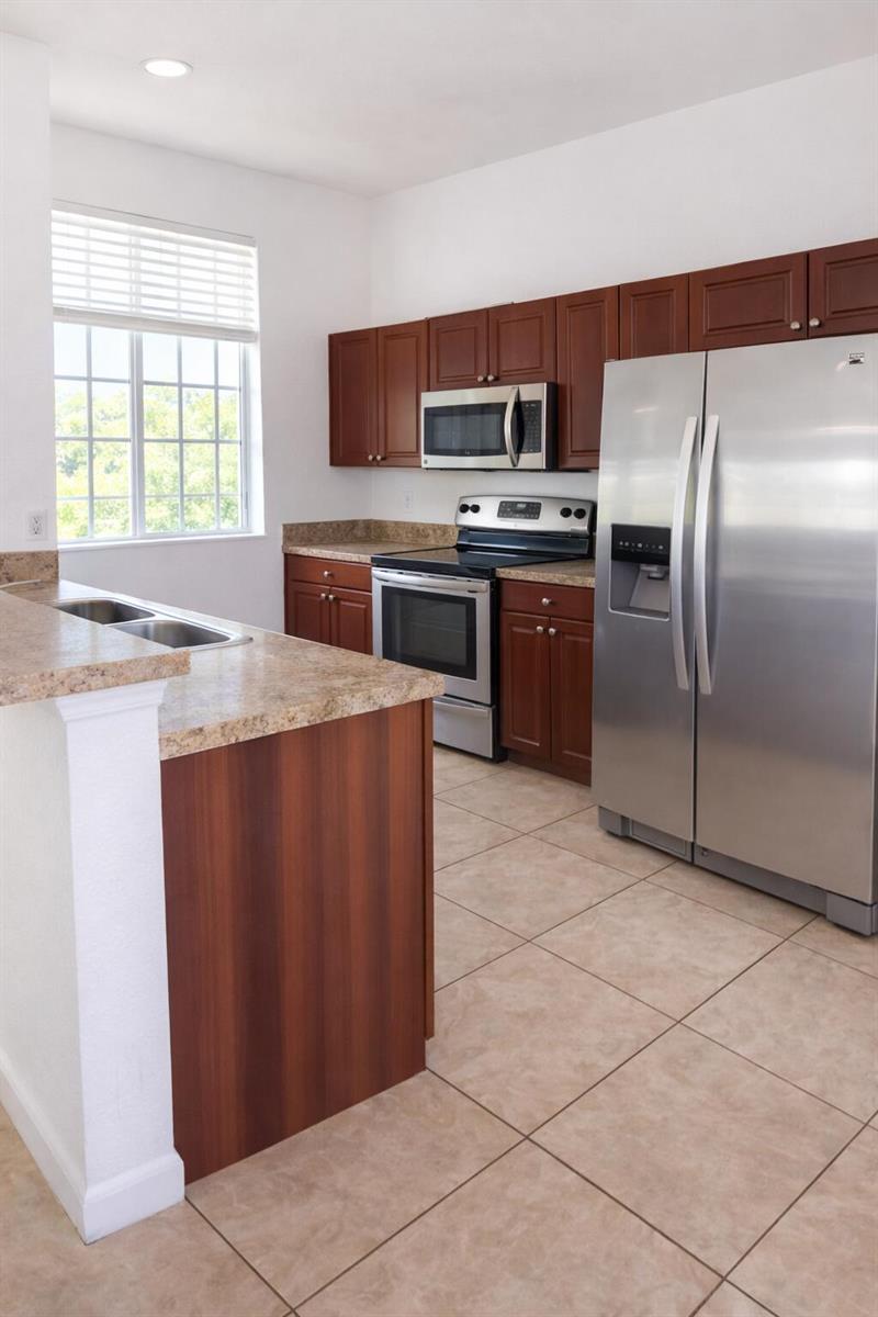 A kitchen features brown cabinets, stainless steel appliances, granite countertops, and light-colored tile flooring — 1219 Lucaya Drive, Riviera Beach FL 33404, RIVIERA BEACH, FL